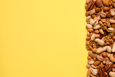 Photo of Different delicious nuts on yellow background, flat lay. Space for text