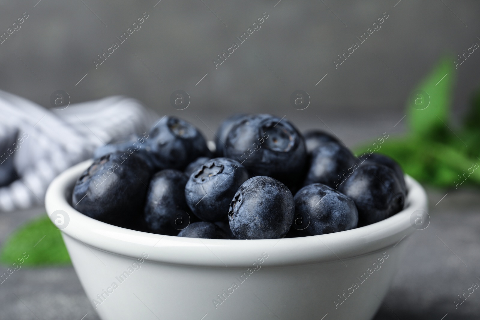 Photo of Bowl of tasty blueberries on grey table, closeup