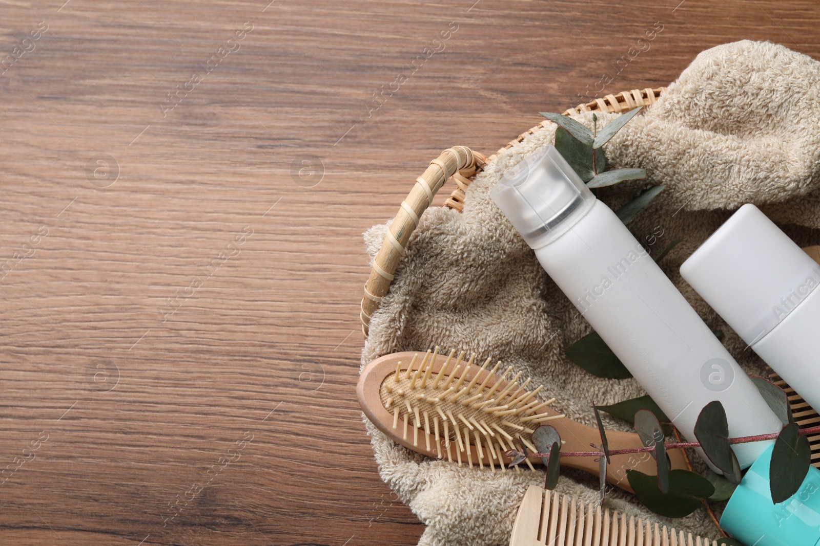 Photo of Dry shampoo sprays, towel and hairbrushes with eucalyptus branch in basket on wooden table, top view. Space for text