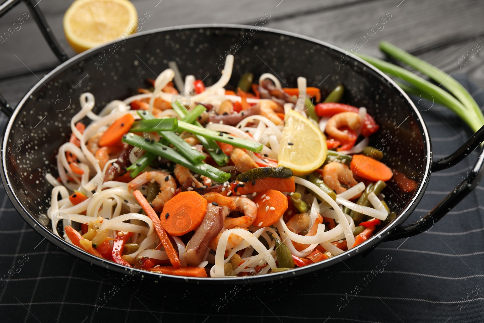 Photo of Shrimp stir fry with noodles and vegetables in wok on black wooden table, closeup