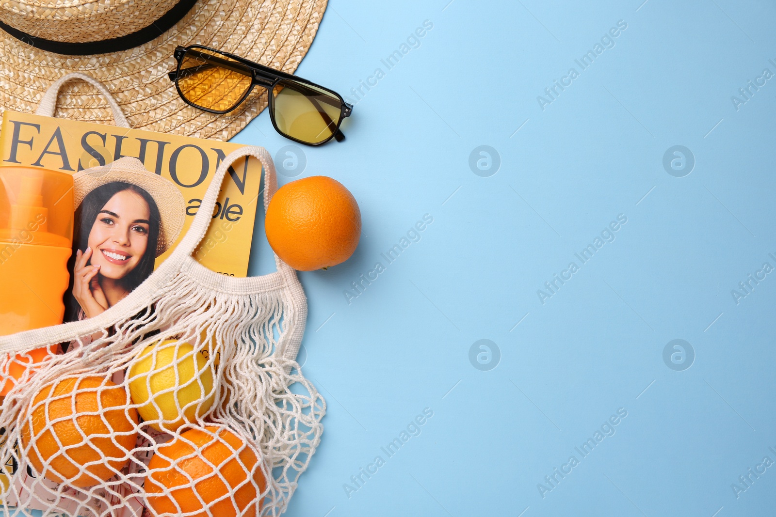 Photo of String bag with magazine, fruits and summer accessories on light blue background, flat lay. Space for text