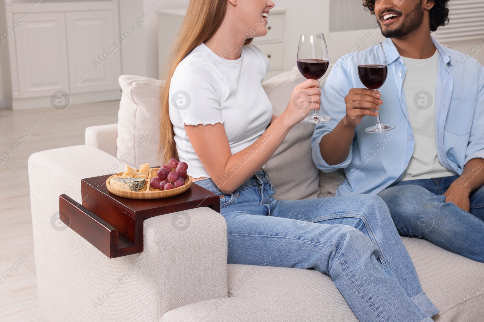 Photo of Grapes and cheese on sofa armrest wooden table. Couple with glasses of wine at home, closeup