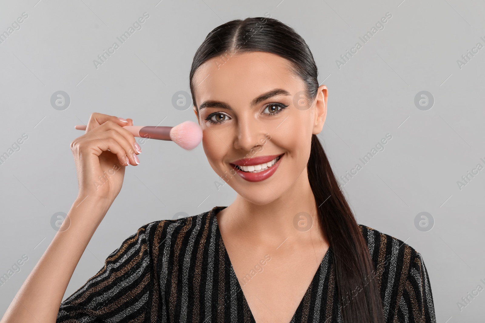 Photo of Everyday makeup. Beautiful woman applying face powder on light grey background