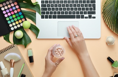 Photo of Young beauty blogger with blush and laptop on light orange background, top view