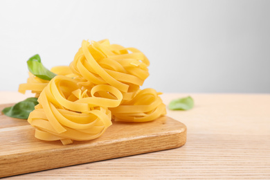 Photo of Uncooked tagliatelle pasta on wooden table against grey background. Space for text
