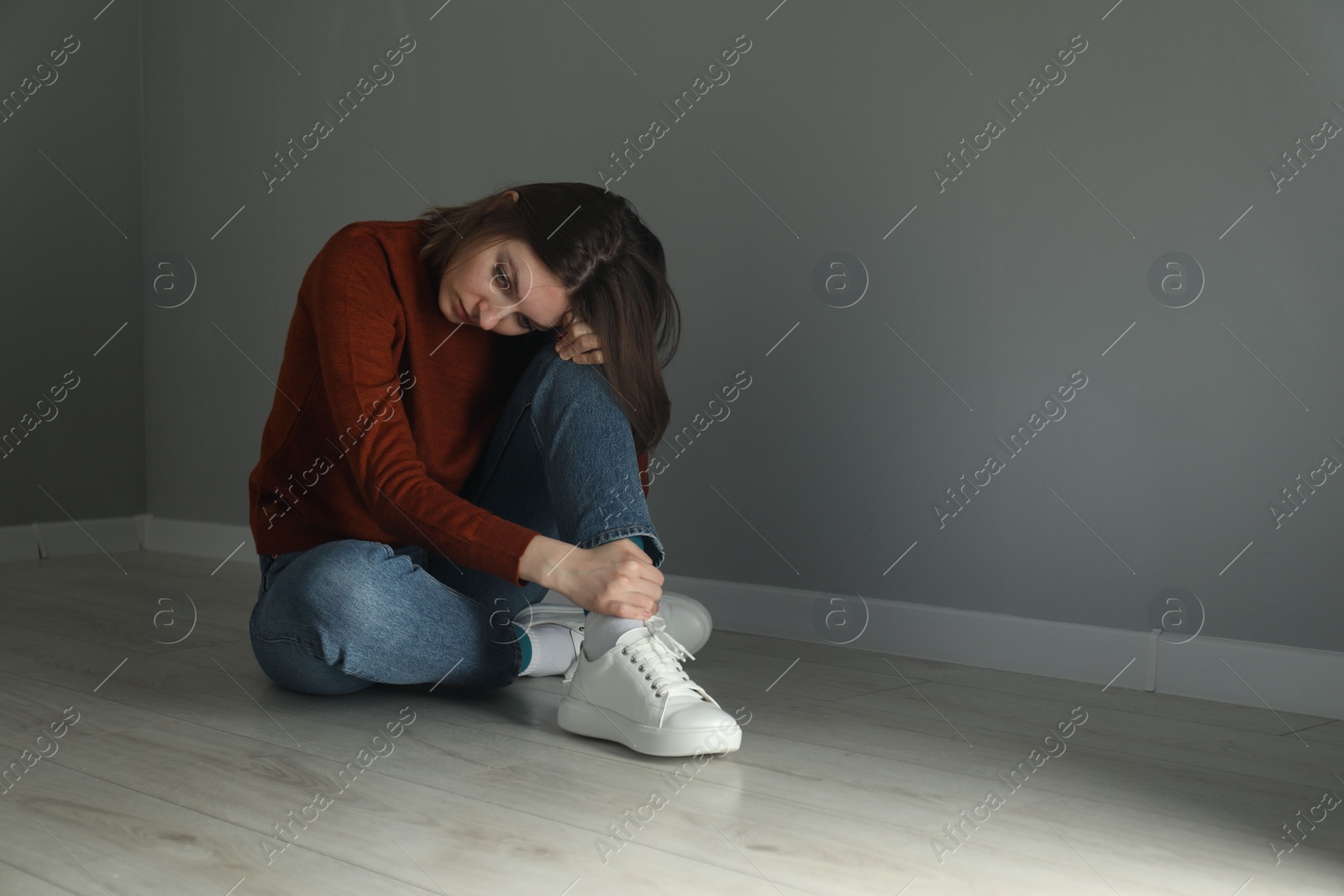 Photo of Sad young woman sitting on floor near grey wall indoors, space for text