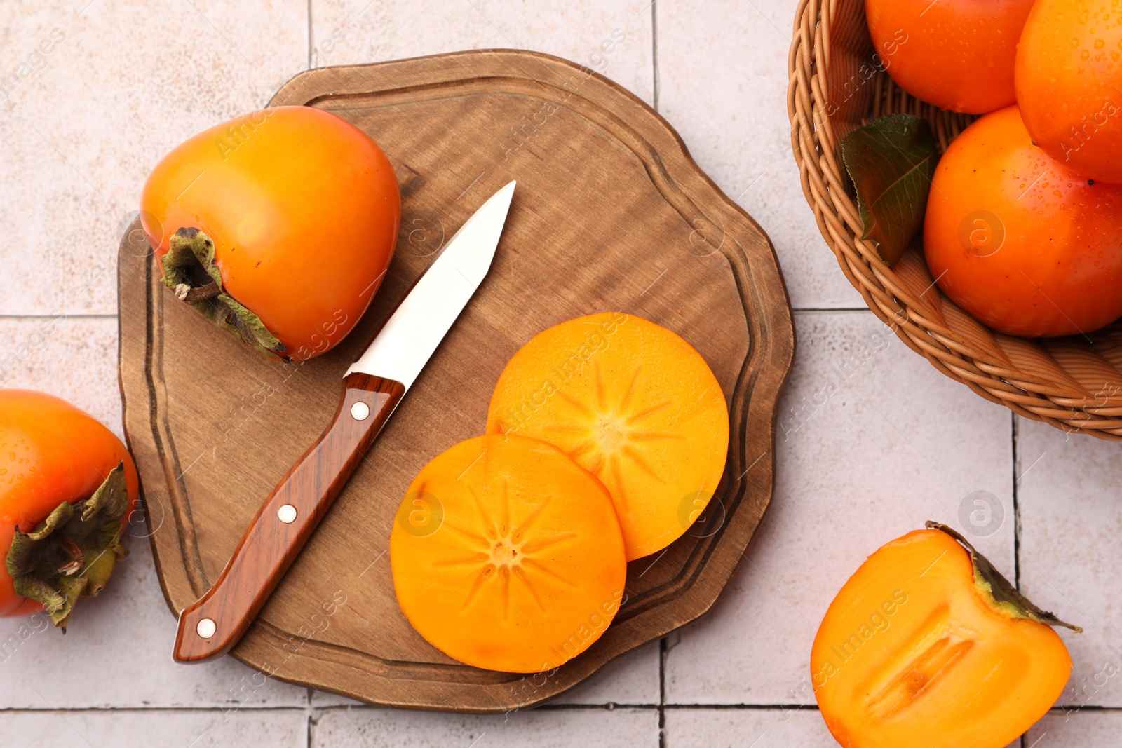 Photo of Delicious ripe juicy persimmons and knife on tiled surface, flat lay