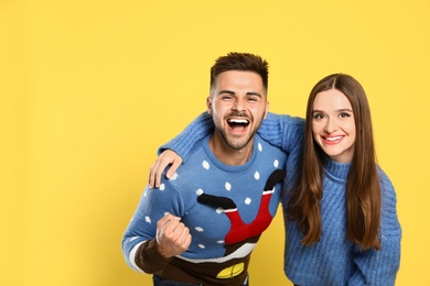 Couple wearing Christmas sweaters on yellow background