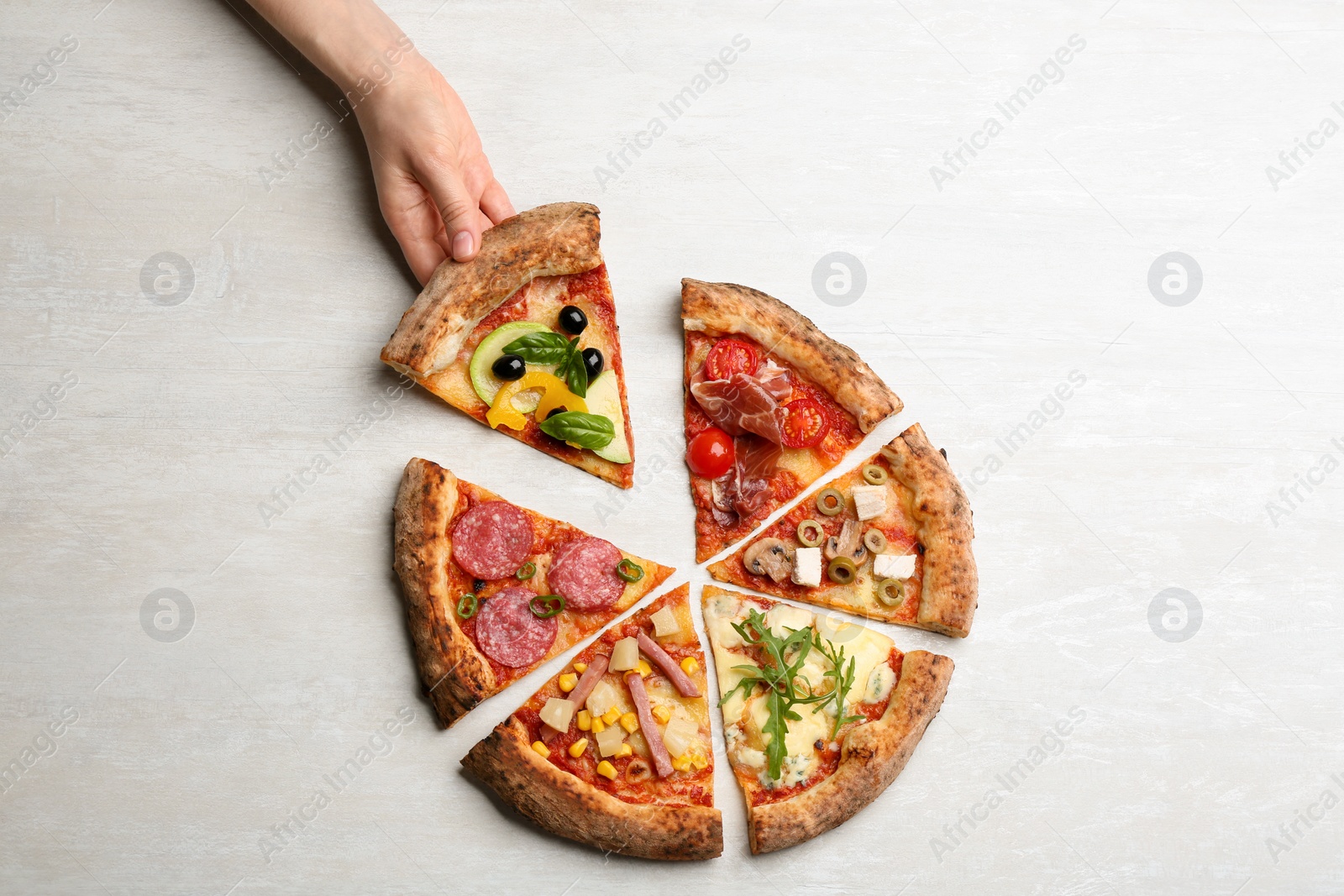 Photo of Woman taking slice of delicious pizza at light grey table, top view