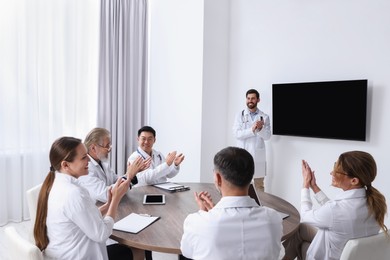 Photo of Teamdoctors listening to speaker report near tv screen in meeting room. Medical conference