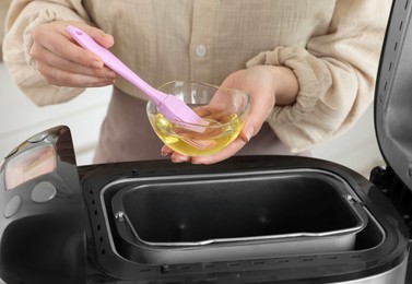 Photo of Woman spreading breadmaker pan with oil, closeup