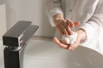 Photo of Woman washing hands with cleansing foam near sink in bathroom, closeup