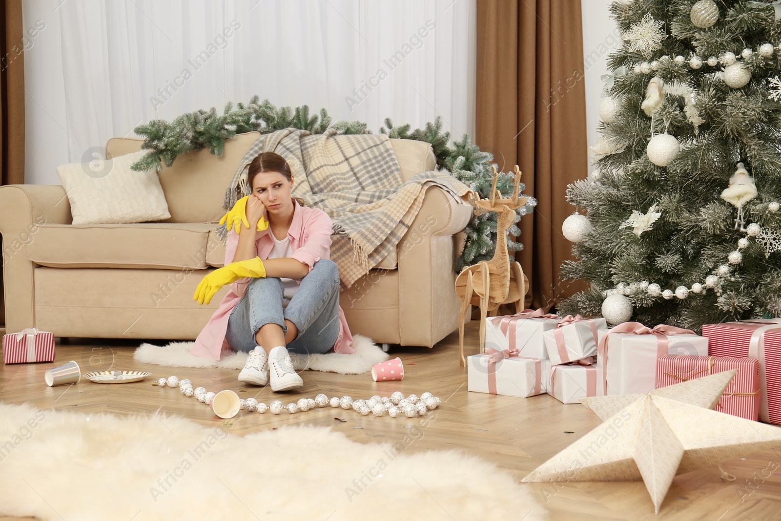 Photo of Tired woman sitting in messy room while cleaning after New Year party