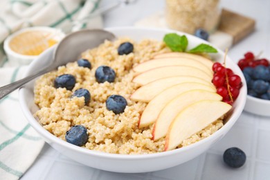 Photo of Bowl of delicious cooked quinoa with apples, blueberries and cranberries on white tiled table, closeup