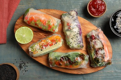 Photo of Many different delicious rolls wrapped in rice paper on blue wooden table, flat lay