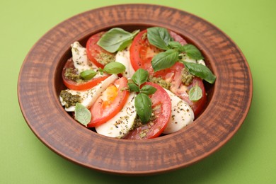 Photo of Plate of delicious Caprese salad with pesto sauce on green table, closeup