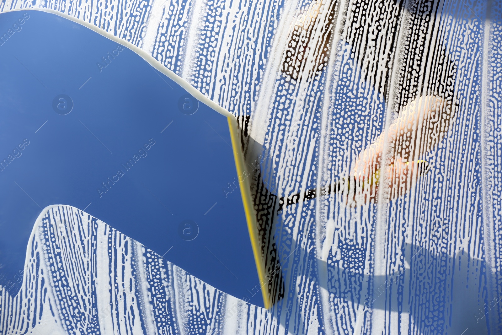 Photo of Woman cleaning glass with squeegee on sunny day, closeup