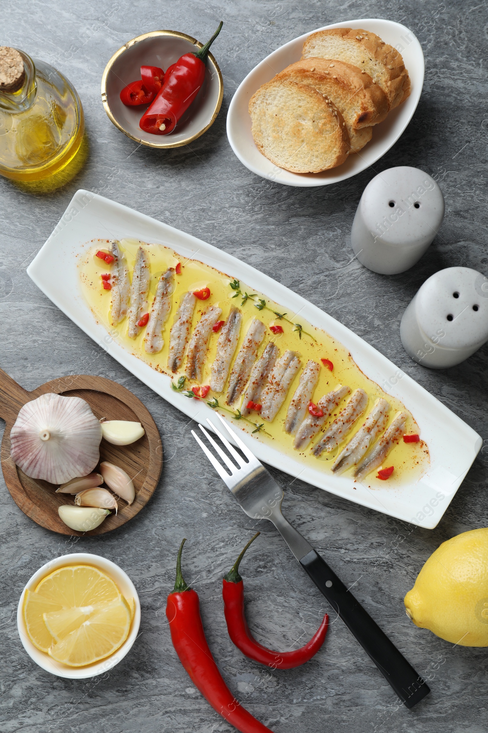 Photo of Tasty pickled anchovies with spices and products on gray table, flat lay