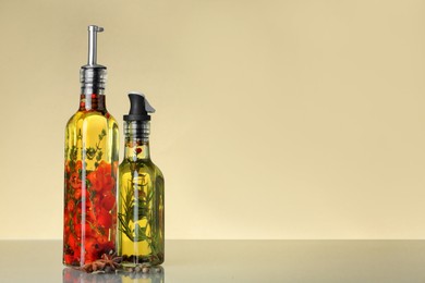 Photo of Cooking oil with different spices and herbs in bottles on beige table. Space for text