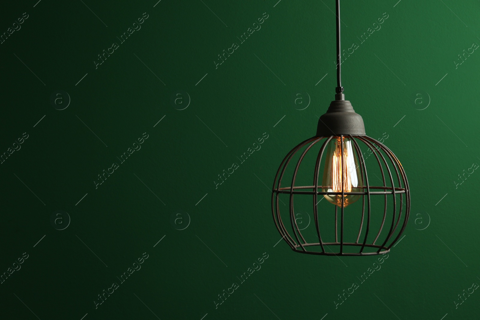 Photo of Hanging lamp bulb in chandelier against green background, space for text