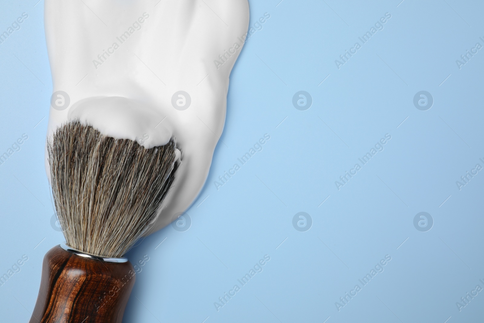 Photo of Brush with shaving foam on light blue background, top view. Space for text