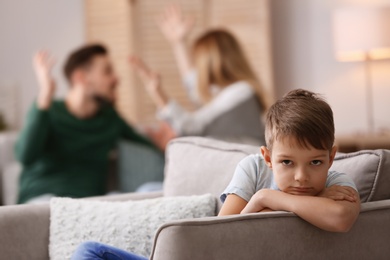 Photo of Little unhappy boy sitting in armchair while parents arguing at home