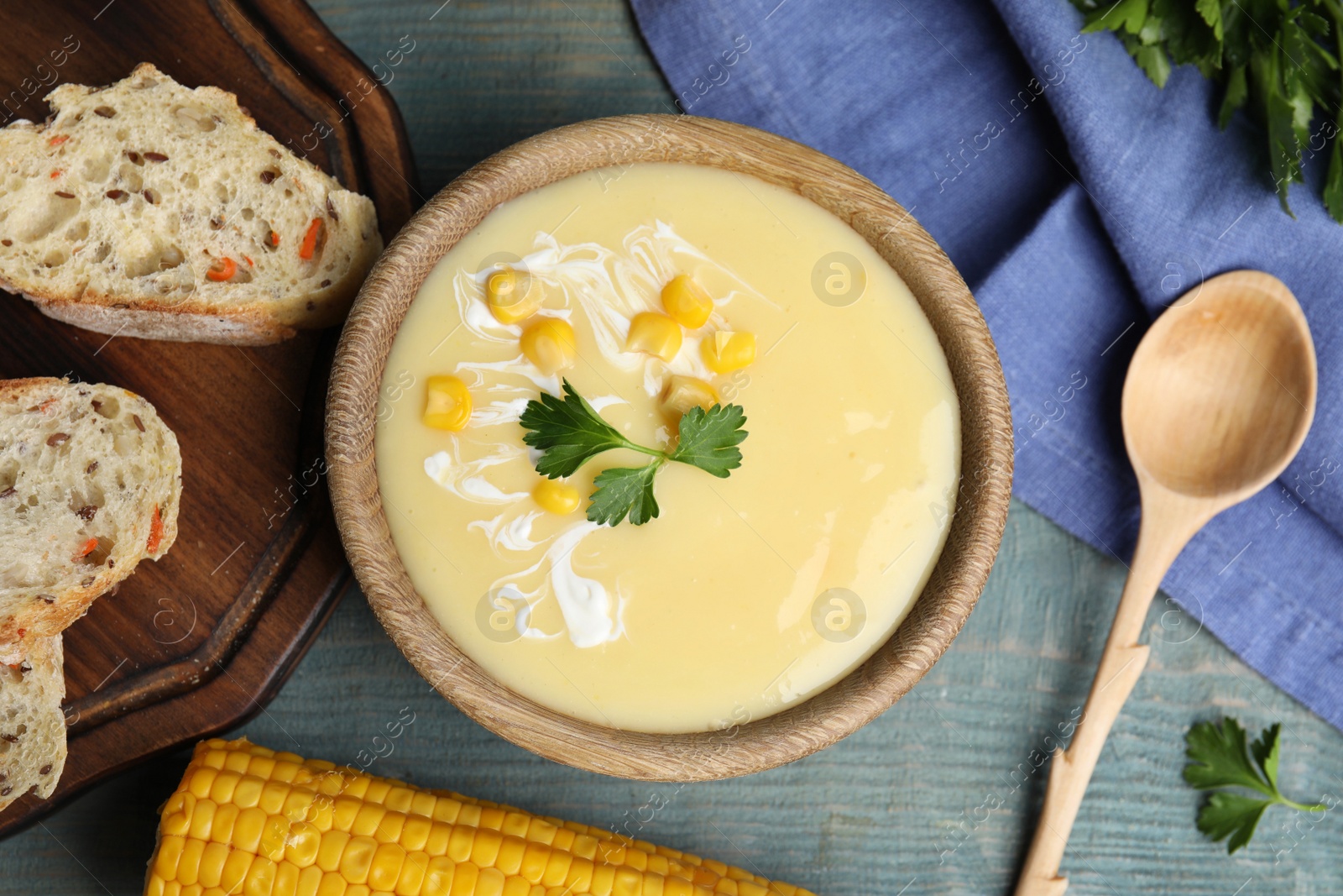 Photo of Delicious corn cream soup served on light blue wooden table, flat lay