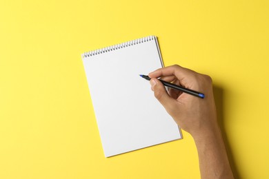 Man with pen and notepad on yellow background, top view