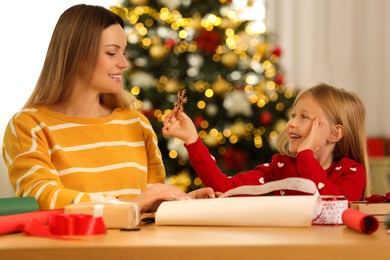 Christmas gifts wrapping. Little daughter showing decorative snowflake to her mother at table in room