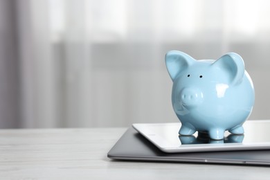 Photo of Piggy bank, tablet and laptop on white table indoors. Space for text