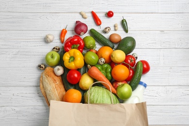 Paper bag with different groceries on white wooden table, flat lay