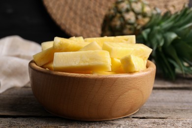 Photo of Pieces of tasty ripe pineapple in bowl on wooden table, closeup