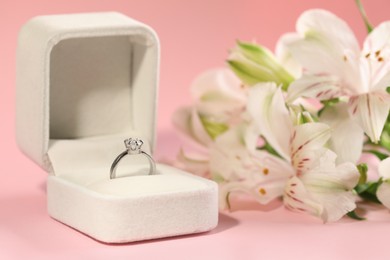 Beautiful engagement ring with gemstone in box and flowers on pink background