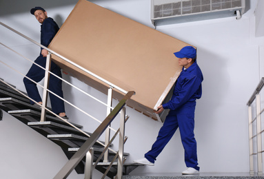 Photo of Professional workers carrying refrigerator on stairs indoors