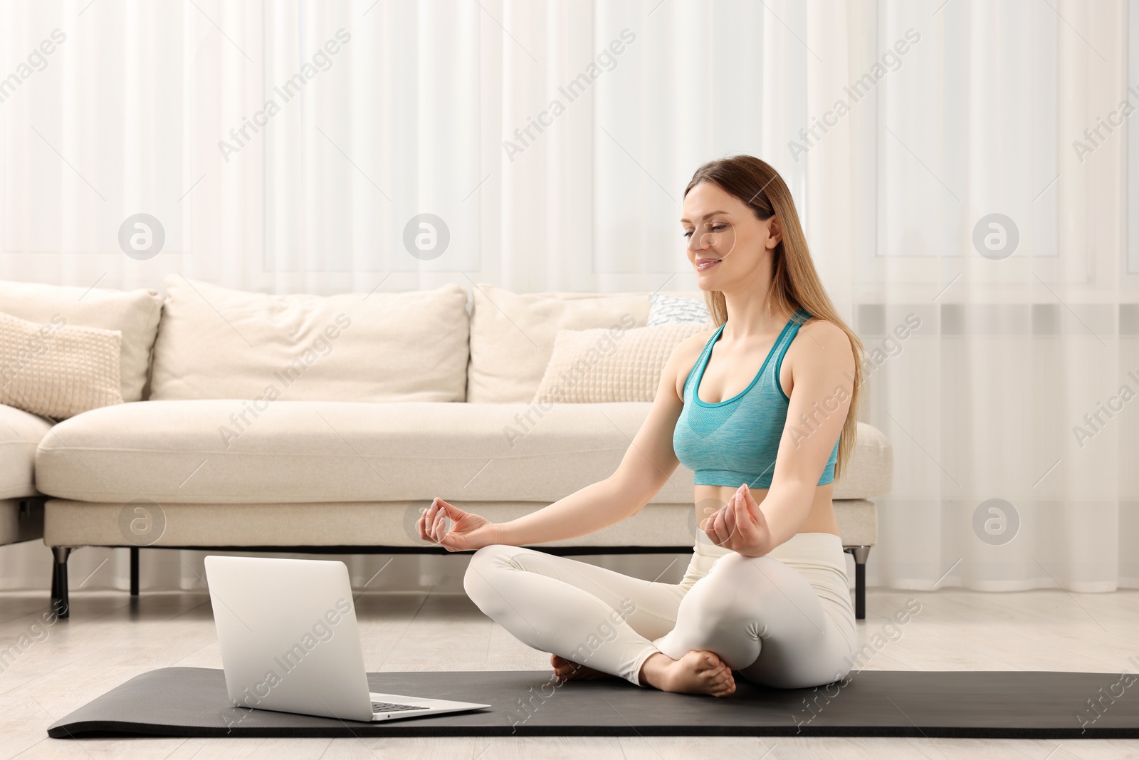 Photo of Woman in sportswear meditating near laptop at home. Harmony and zen