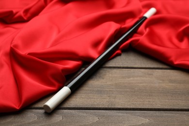 Photo of Beautiful black magic wand and red fabric on wooden table
