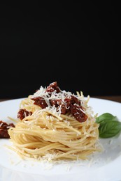 Tasty spaghetti with sun-dried tomatoes and parmesan cheese on plate against black background, closeup. Exquisite presentation of pasta dish