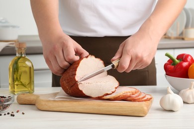 Photo of Man cutting delicious ham at white wooden table indoors, closeup