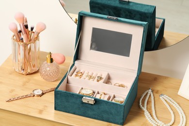 Photo of Jewelry box with many different accessories, perfume and makeup brushes on wooden table