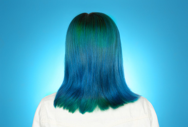 Woman with bright dyed hair on light blue background, back view