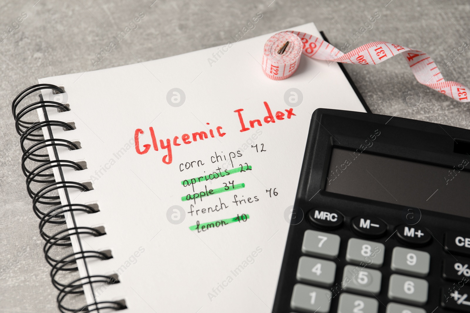 Photo of Glycemic Index. Notebook with information, measuring tape and calculator on light grey table, closeup