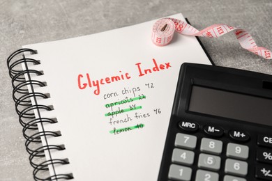 Glycemic Index. Notebook with information, measuring tape and calculator on light grey table, closeup