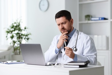 Doctor having online consultation via laptop at table in clinic