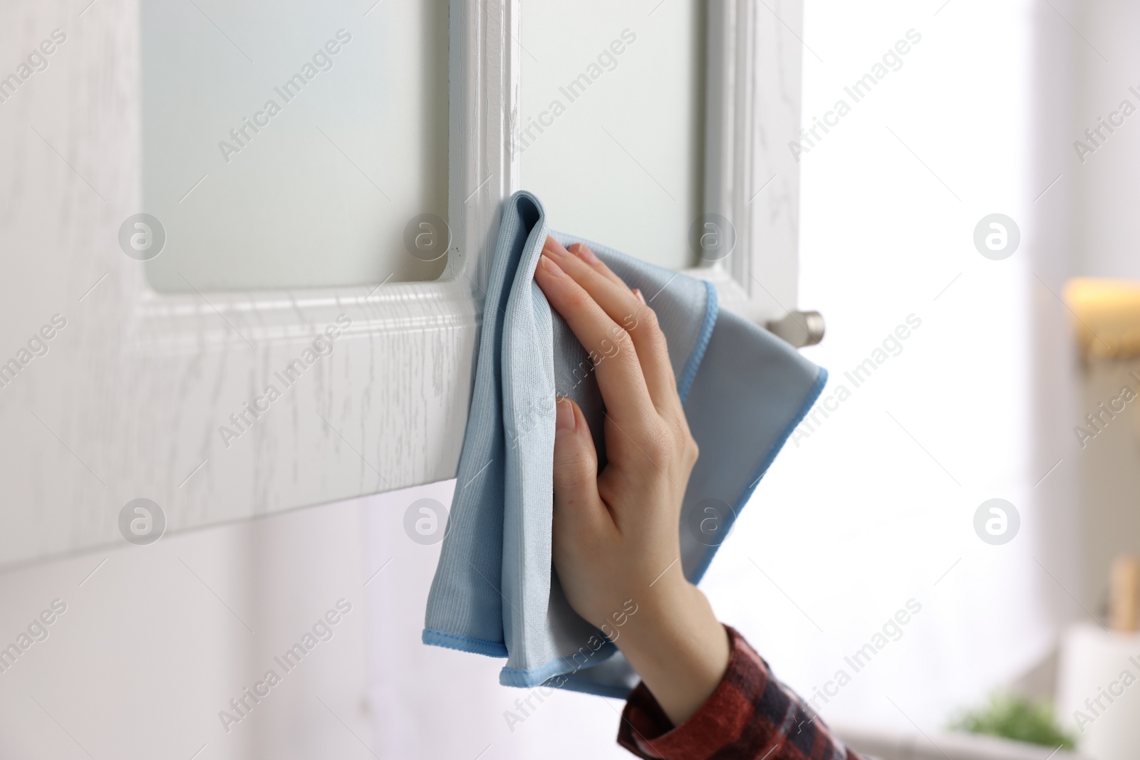 Photo of Woman with microfiber cloth cleaning white cabinet in kitchen, closeup