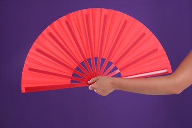 Photo of Woman holding red hand fan on purple background, closeup