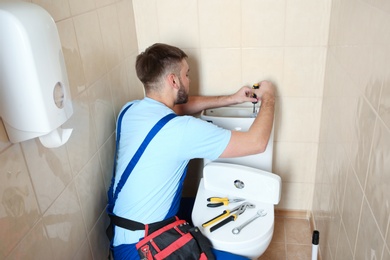 Photo of Professional plumber in uniform repairing toilet tank indoors