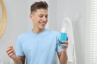 Young man with mouthwash and toothbrush in bathroom