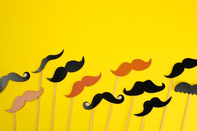 Photo of Fake paper mustaches with sticks on yellow background, flat lay. Space for text