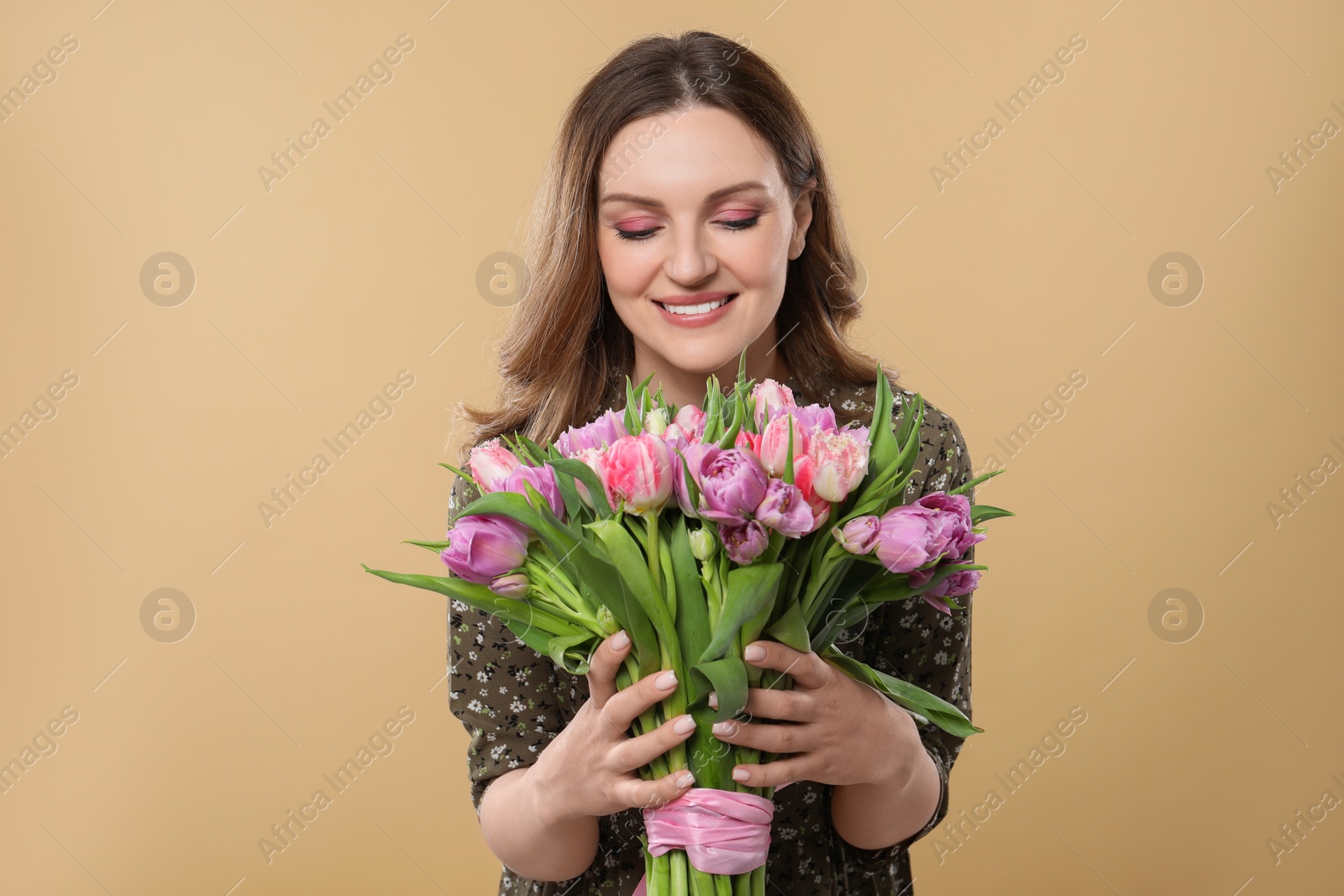Photo of Happy young woman holding bouquet of beautiful tulips on beige background