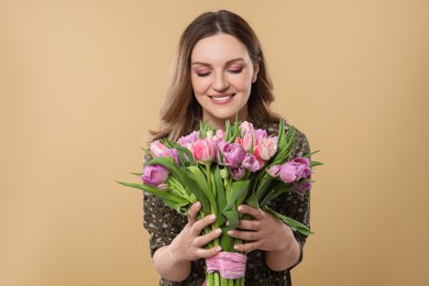 Happy young woman holding bouquet of beautiful tulips on beige background